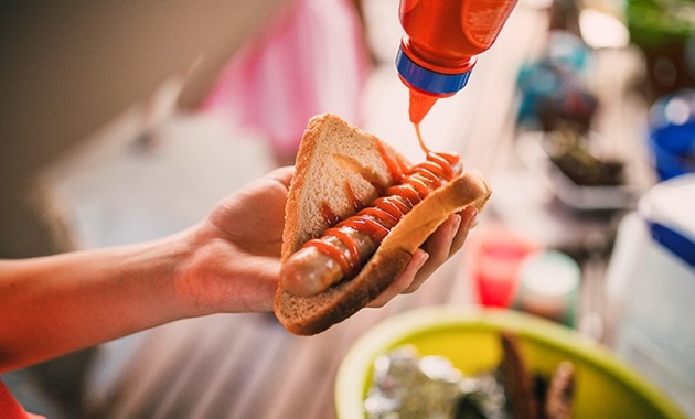 Image of person's hand holding piece of bread with barbecued sausage