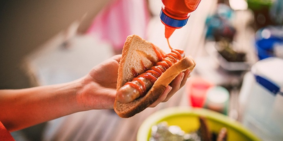 Image of person's hand holding piece of bread with barbecued sausage