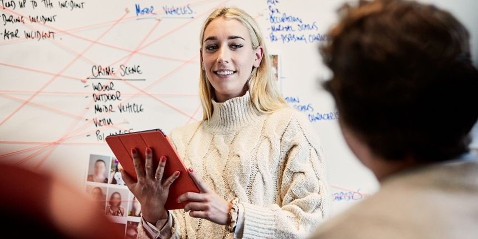 Student stands in front of whiteboard holding a clipboard