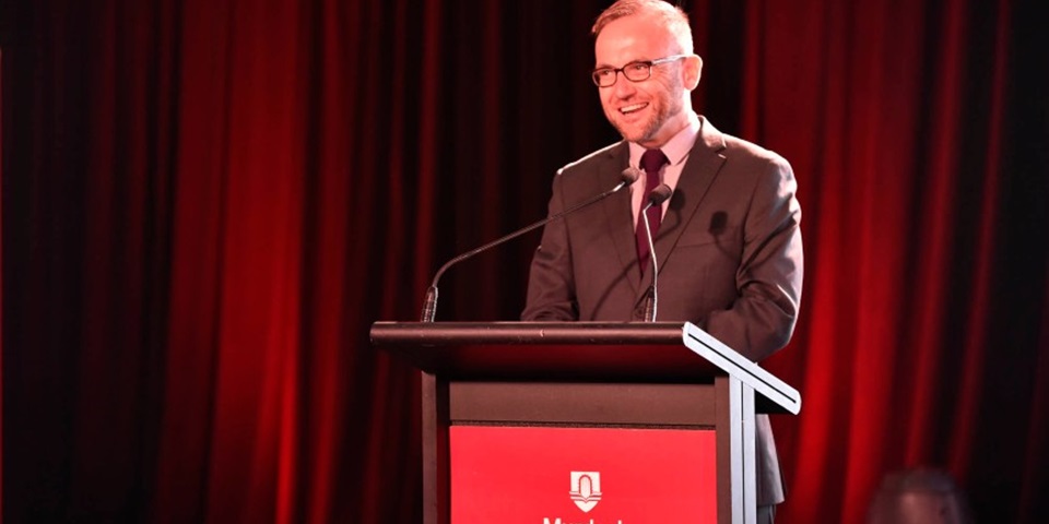 Adam Bandt in brown suit giving a speech on a Murdoch University podium