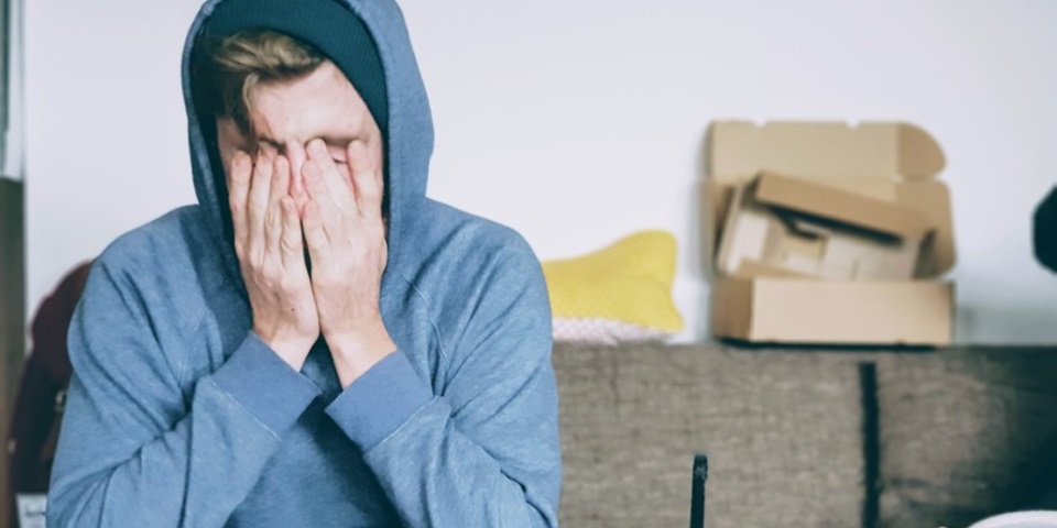 man in blue hoodie with his face in his hands