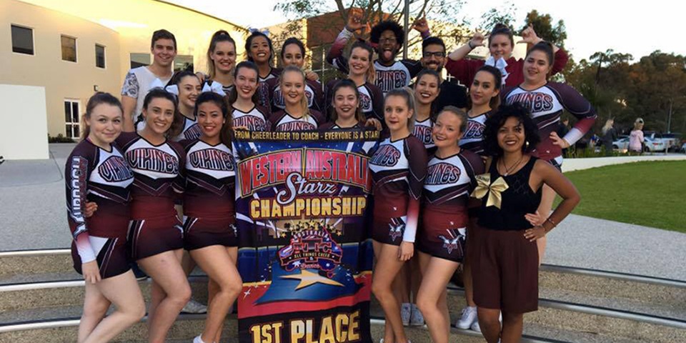 18 members of the Murdoch University Cheerleading Team in uniform, smiling and posing with a 1st place banner