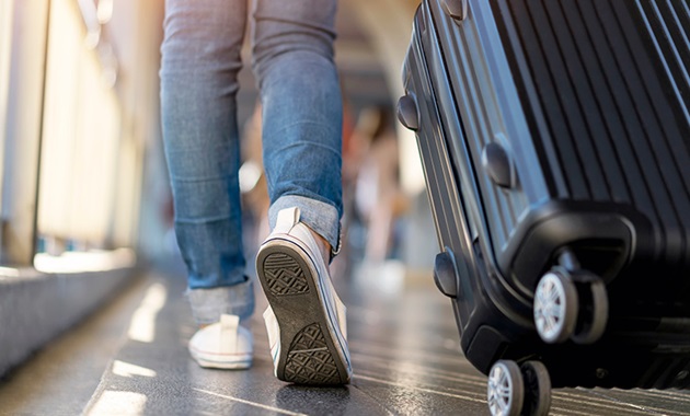 Shot of legs in jeans and white converses walking in airport with a suitcase