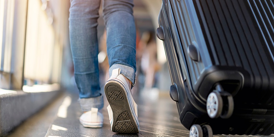 Shot of legs in jeans and white converses walking in airport with a suitcase