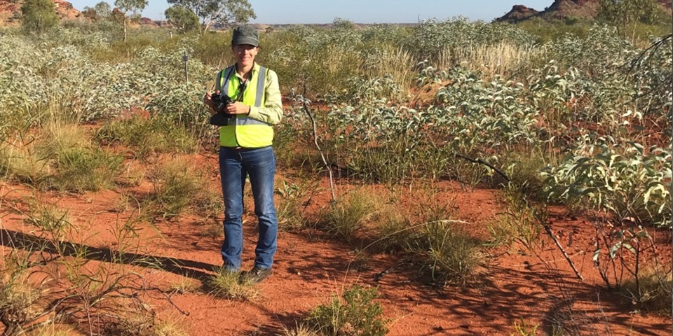 Associate Professor Rachel Standish standing in a red earth field with native shrubs