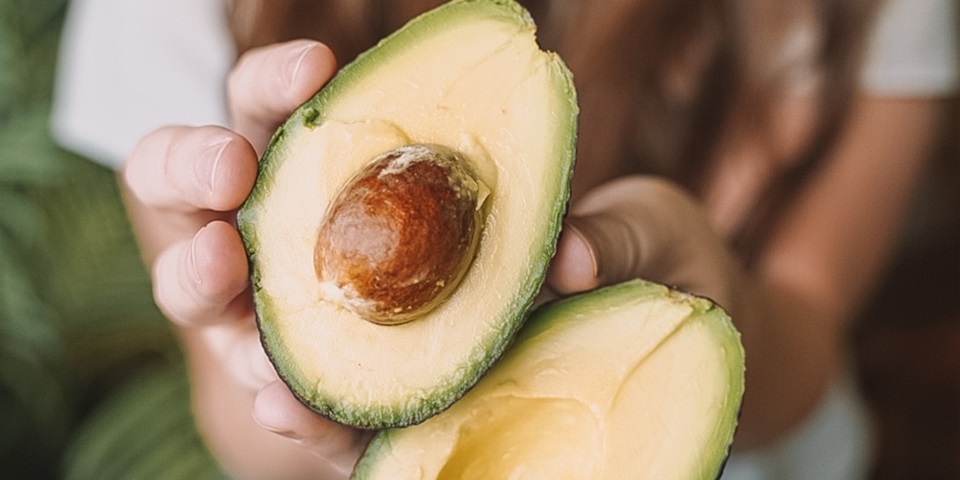 Girl holding halved avocado up to camera