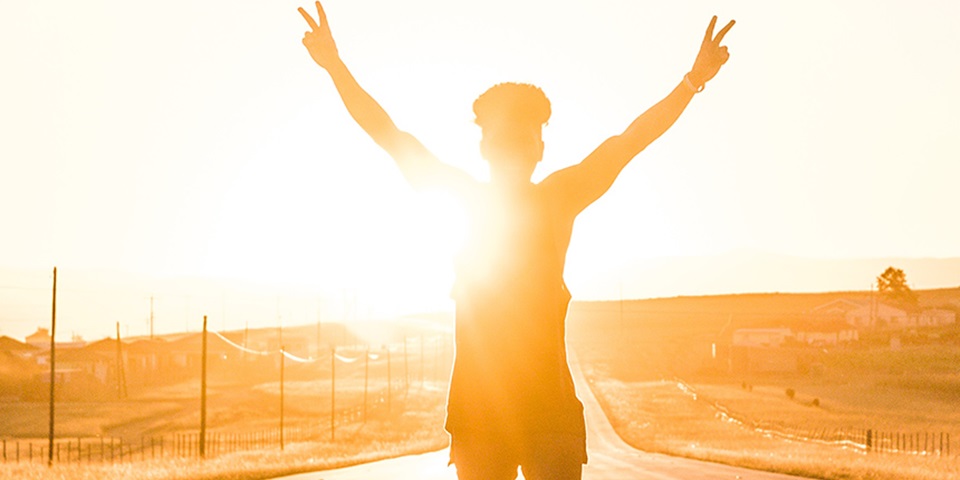 Boy standing on the road with his hands in the air and the sun setting behind him