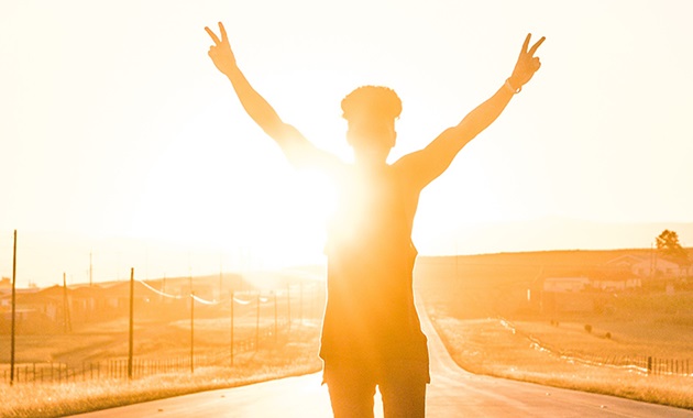 Boy standing on the road with his hands in the air and the sun setting behind him