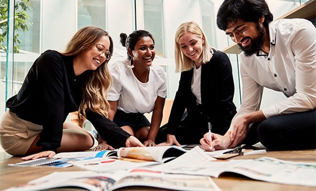 Four students sitting on the floor, smiling over an assortment of documents.