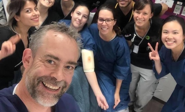 A group of Murdoch nursing students in scrubs smile to camera with their lecturer