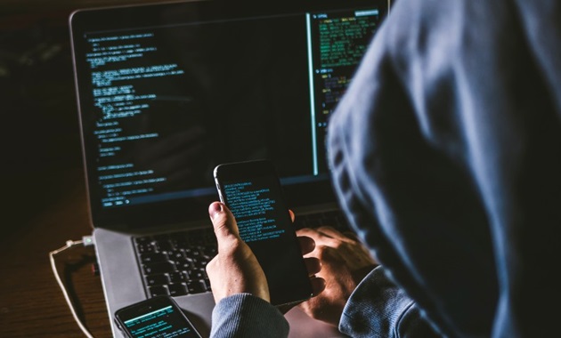 mysterious man in hoodie on his computer and phone