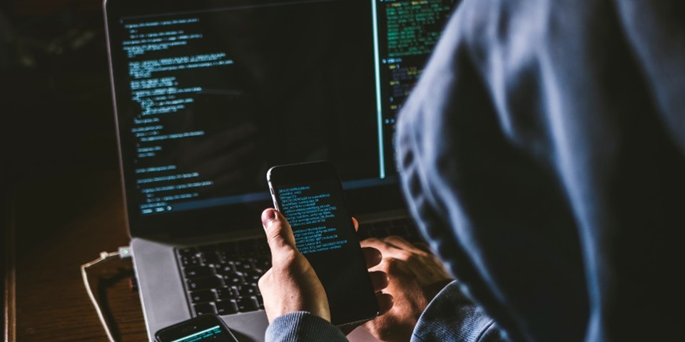 mysterious man in hoodie on his computer and phone