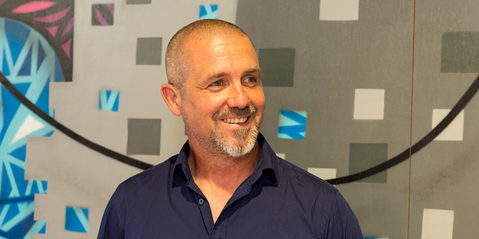 Academic Ian Wilson smiling to someone off camera with graffiti in background