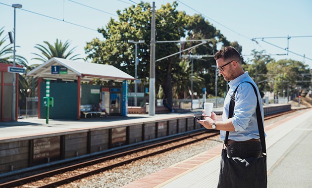 Man with a bag and coffee waiting at a Perth train station