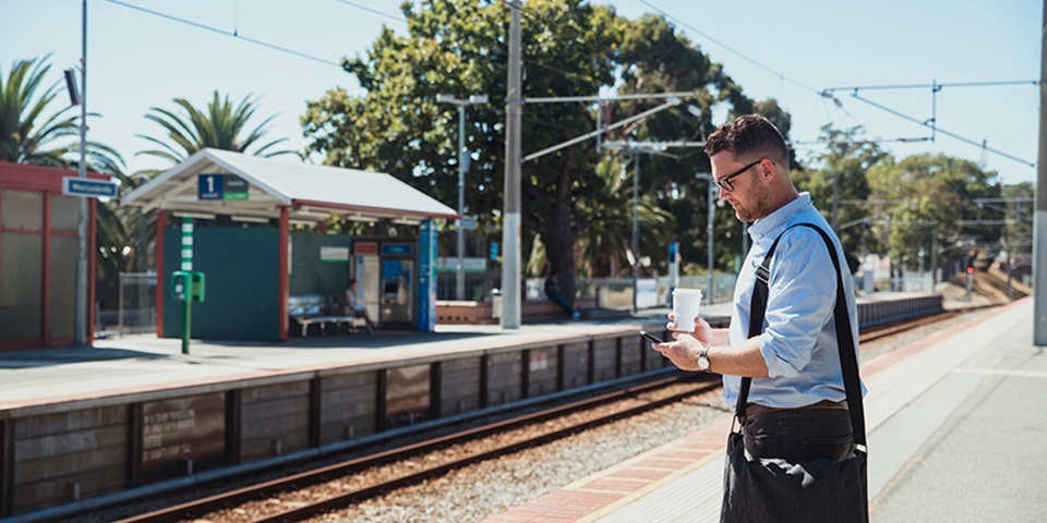 Man with a bag and coffee waiting at a Perth train station