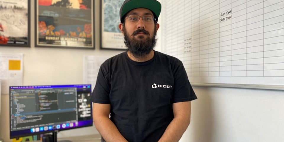 Gursimar Singh standing in front of computer with hands crossed looking to camera