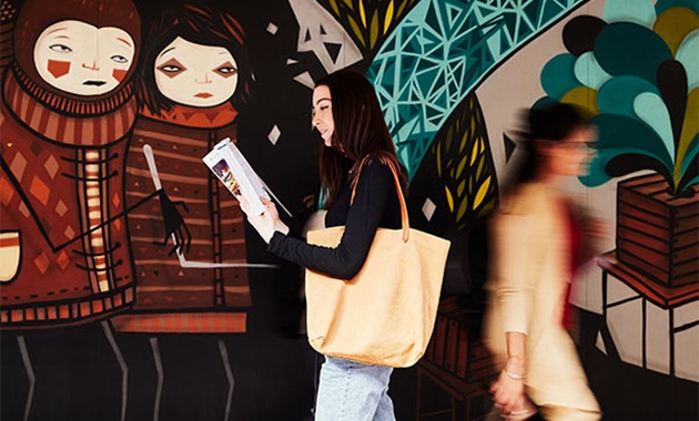 Female student reading book and walking past graphic wall.