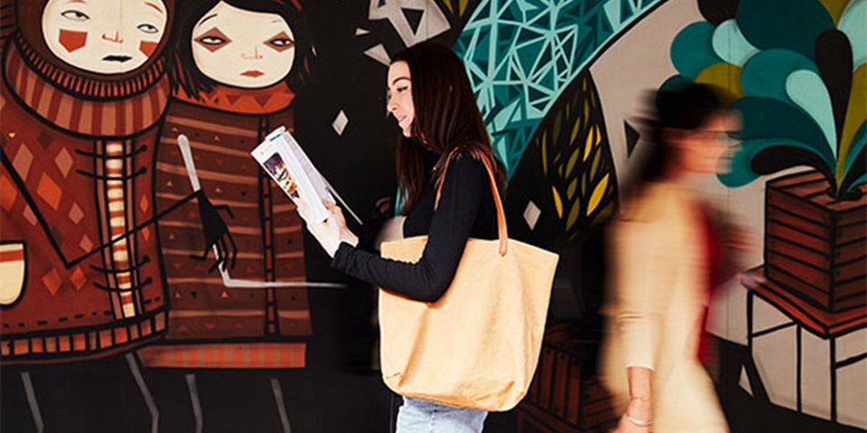 Female student reading book and walking past graphic wall.