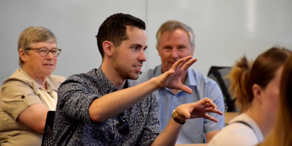 Student presenting to room in front of two people looking on