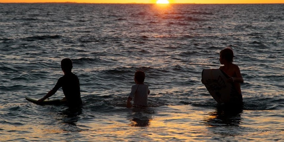 Three young people swimming in the ocean at sunset.