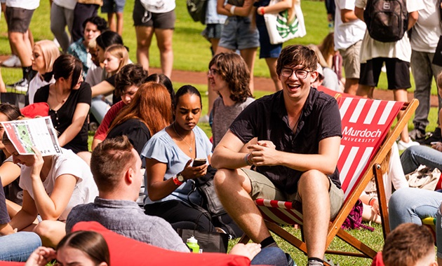 Image of student sitting on deckchair on Bush Court, smiling to a friend