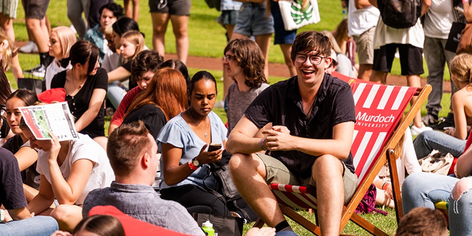 Image of student sitting on deckchair on Bush Court, smiling to a friend