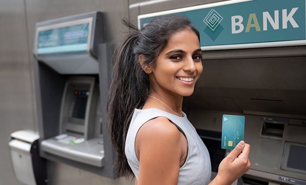 Female student smiling in front of ATM holding up a debit card