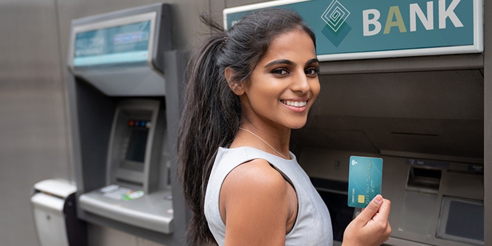 Female student smiling in front of ATM holding up a debit card