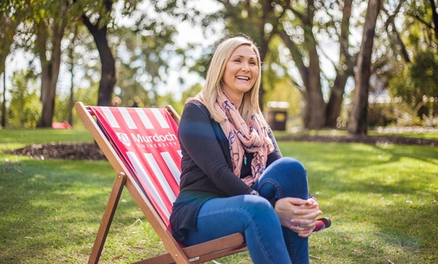 Joanne sitting on bush court at Murdoch University smiling