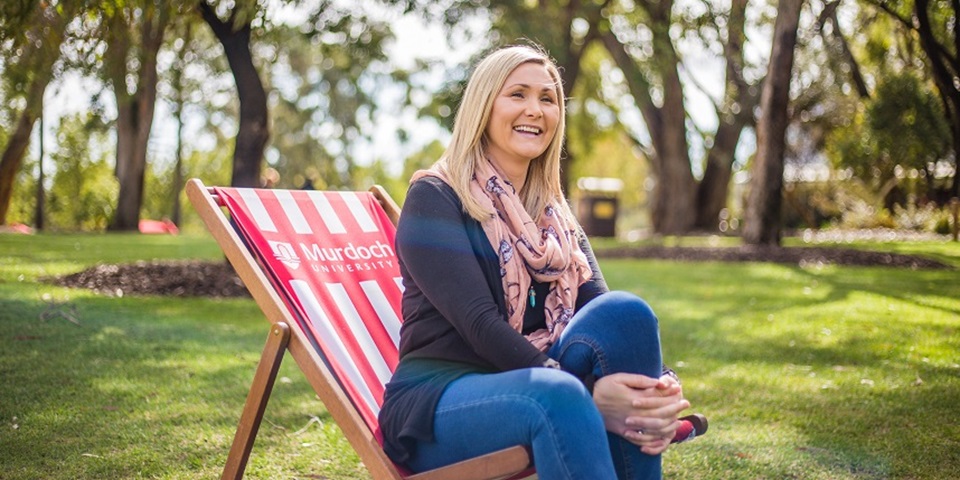 Joanne sitting on bush court at Murdoch University smiling