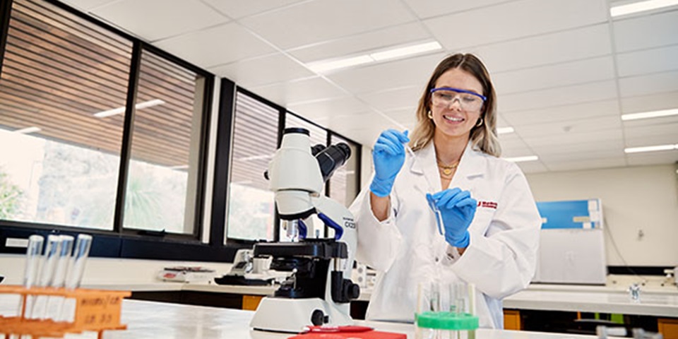 Female student in lab coat works in laboratory.