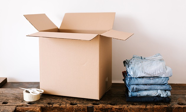 Folded jeans next to an open cardboard box on a wooden table