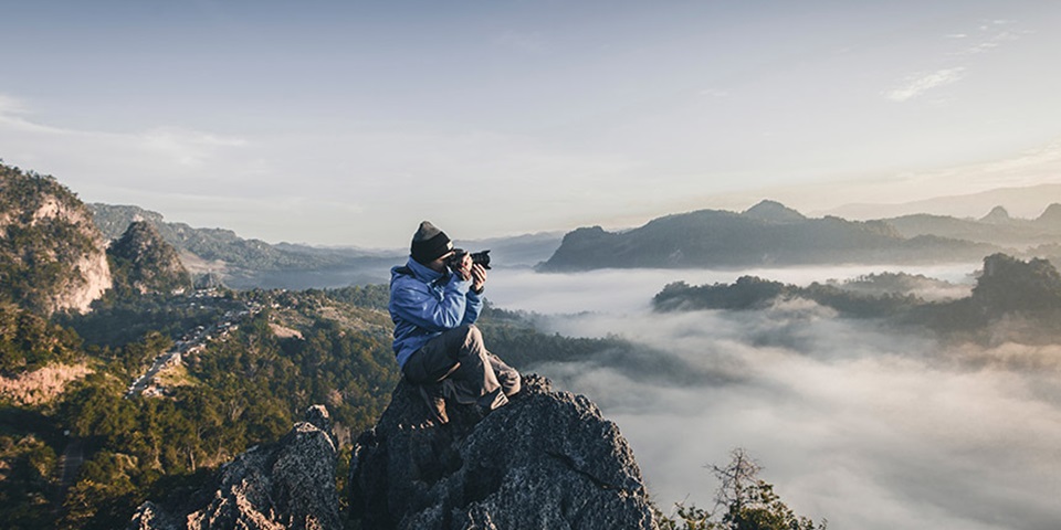 Man taking a photo at the top of a misty mountain range