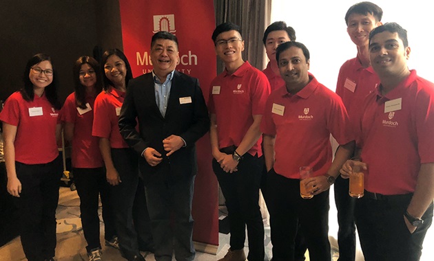 Spencer Teng stands with a group of alumni in front of a Murdoch University banner