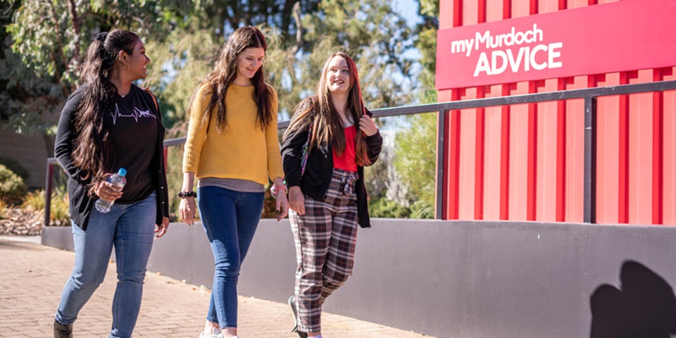 Three students walking near an advice hub