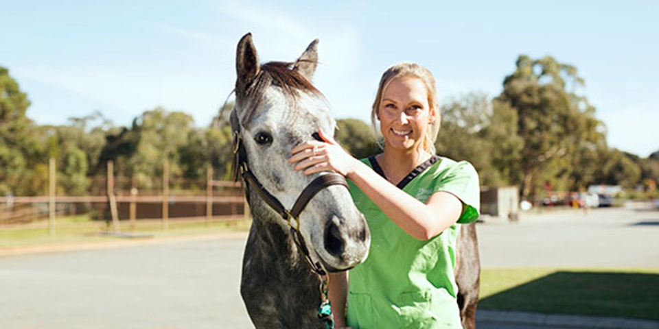 Female student standing next to a horse, smiling.