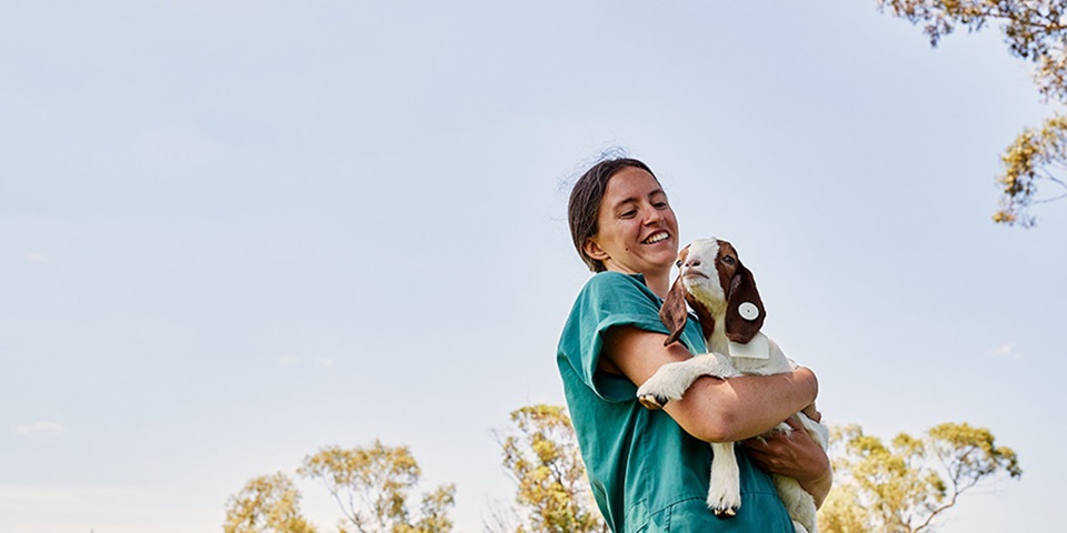 Female student holding a small goat, smiling.