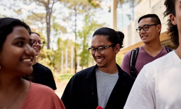 Close up of group of students walking through campus, student in middle is in focus and is smiling off camera