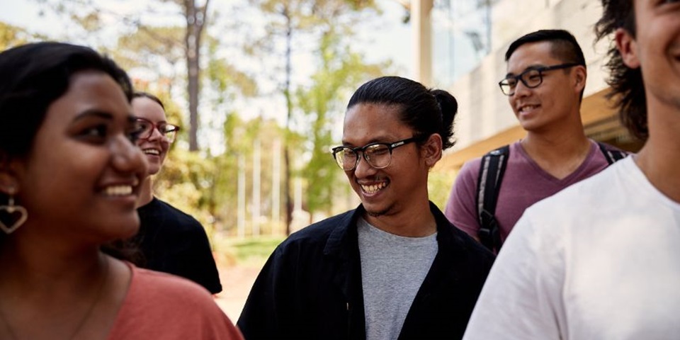 Close up of group of students walking through campus, student in middle is in focus and is smiling off camera