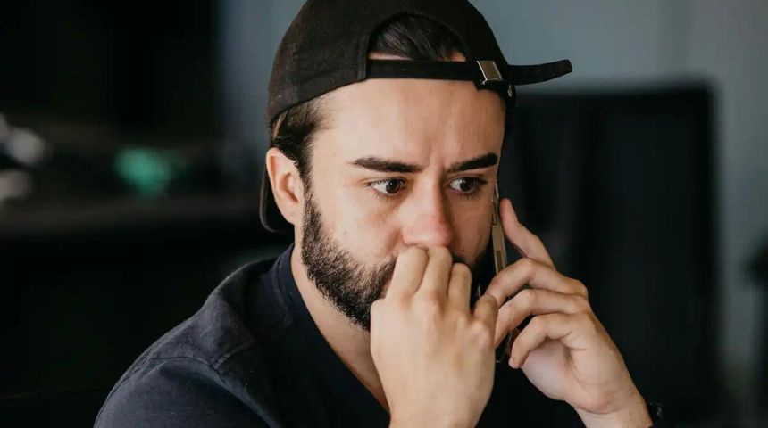 Image of a young man looking worried as he holds a mobile phone to his ear.